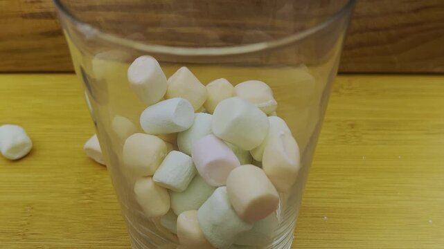 Colorful marshmallows filling clear glass for sweet snack or dessert preparation showcasing soft confectionery pastel colors and playful food presentation