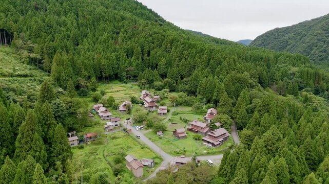 Aerial view of traditional houses in the Ozuchi historic district surrounded by lush green forests in Kaga, Ishikawa, Japan.