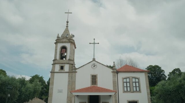 Whitewashed parish church with a granite bell tower cross and clock face in Portugal