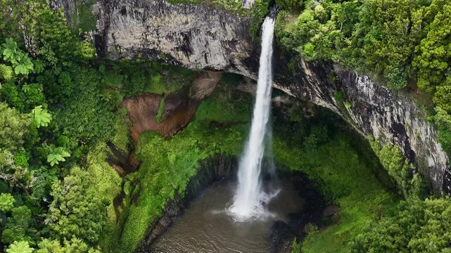 Bridal Veil Falls near Raglan, New Zealand, drops from basalt cliffs into deep pool surrounded by lush native forest, Waikato waterfall scenery.