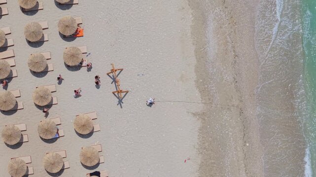 Aerial view of Kroreza Beach with rows of straw umbrellas, sun loungers, and people relaxing on the sand by the turquoise sea in Sarande, Vlore County, Albania.