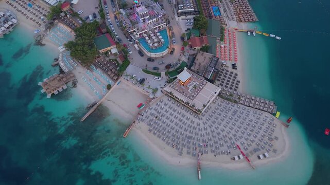 Aerial view of a beach resort in Ksamil with rows of sun loungers, umbrellas, and a swimming pool overlooking the turquoise Ionian Sea in Ksamil, Vlore County, Albania.