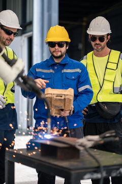 Robotic Welding Team Operating an Automated Robot Arm as Three Workers Observe Bright Sparks on a Metal Worktable in a Factory