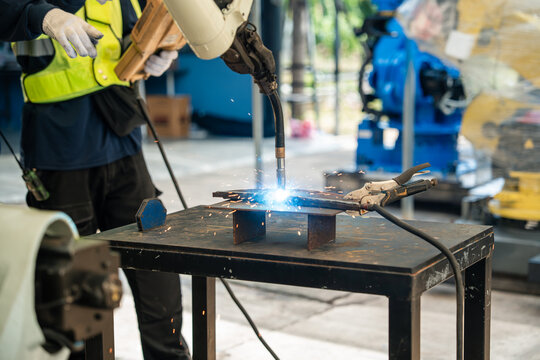 Robotic Welding System Joining Metal Components on a Worktable with Bright Arc Light and Sparks in an Industrial Workshop