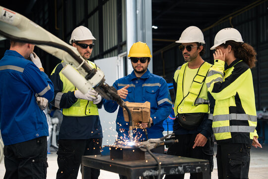 Engineering Team Attending a Robotic Welding Demonstration with Sparks from an Automated Robot Arm in a Manufacturing Workshop