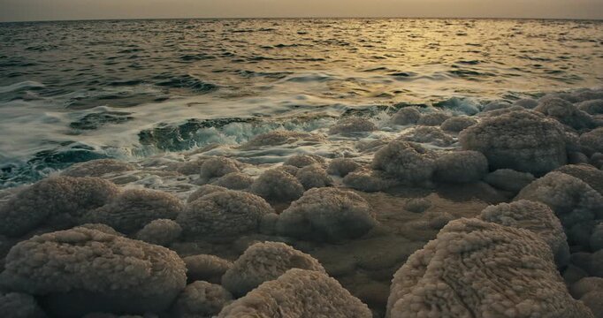 Close up of natural salt formations along the shoreline of the Dead Sea in Jordan. Gentle waves, warm sunset light, and textured mineral deposits create a dramatic and tranquil natural landscape.
