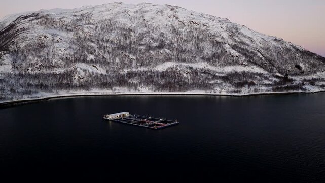 Polar night aerial view over cod farm marine pens in Ringvassoya in snowy winter
