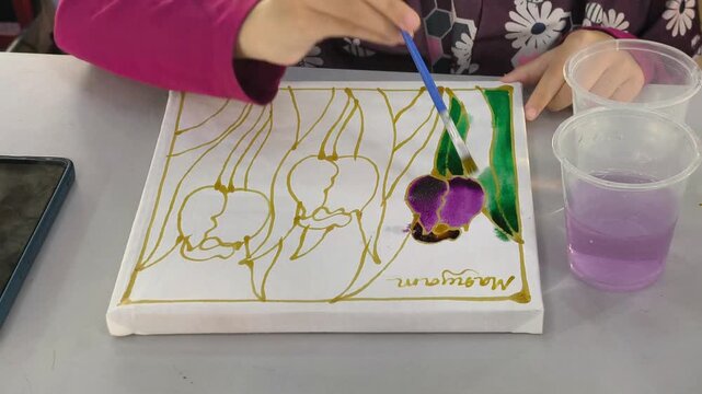 Close-up of a child painting colorful dye on a traditional Malaysian batik canvas. Young student learning cultural heritage craft through hands-on art. Educational activity introducing authentic folk