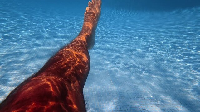 The legs of an adult man practicing swimming kicks inside of a swimming pool in slow motion.
