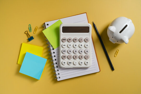 Personal finance planning with piggy bank, calculator and notebook on yellow background, flat lay