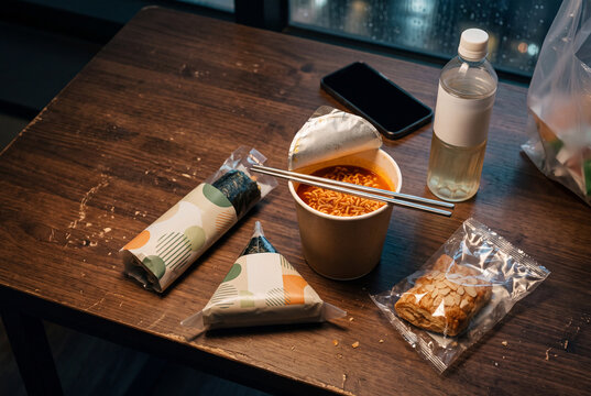 Takeaway ramen cup rice triangles on wooden table with snack water bottle and chopsticks for casual meal background and food banner design