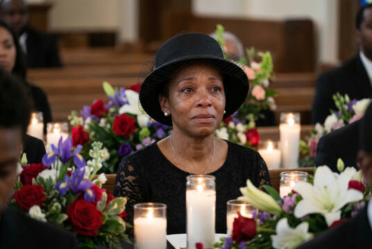 A poignant farewell capturing a petite Black woman in mourning attire, surrounded by flourishing flowers and soft candlelight