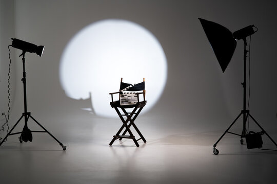 Director chair with movie clapperboard under spotlight with lighting equipment in a modern photo studio