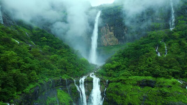 4K Aerial shot of Nanemachi waterfall flowing from mountain cliff during heavy rain in Western Ghats, Maharashtra, India. Beautiful waterfall surrounded by monsoon clouds and lush green forest. 