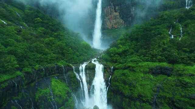 4K Aerial view of Nanemachi Waterfall flowing through dense green forest, surrounded by dramatic misty hills and multiple cascading streams in the Western Ghats of Maharashtra. Landscape of India. 