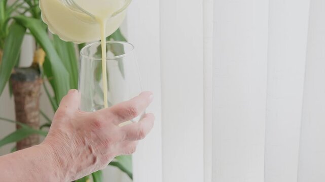 Older person pouring healthy smoothie into glass for breakfast