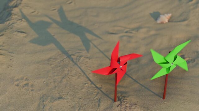 Two colorful pinwheels spinning on a sandy beach with shadows