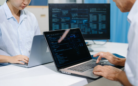 Two software developers collaborating with laptop and tablet, reviewing source code and digital dashboards in a modern office for programming and software development.