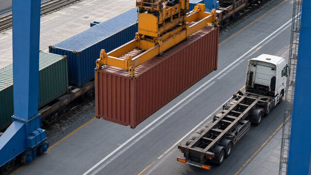 Container crane loading a cargo container onto a truck beside freight trains. Intermodal dry cargo terminal logistics and international transportation infrastructure.