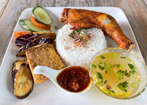 Traditional Indonesian ayam penyet meal served with fried chicken, steamed rice, vegetables, tofu, soup, and spicy sambal.