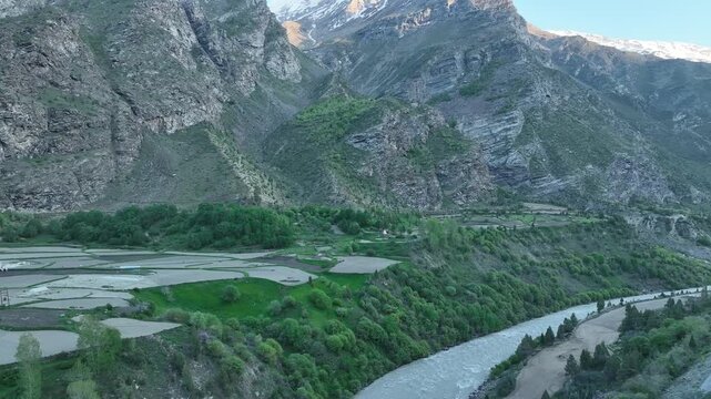 Aerial view of white Buddhist stupa monument surrounded by green trees and farm fields near a river gorge near Jispa Lahaul Valley shot by a drone