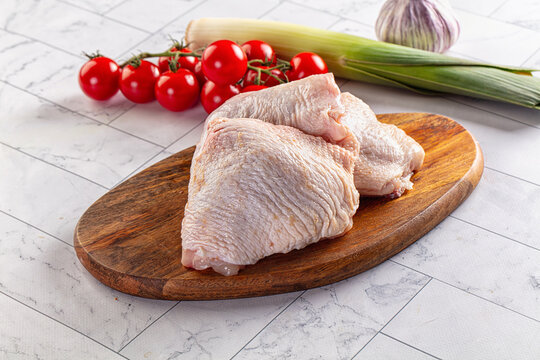 Raw chicken thighs on wooden cutting board with cherry tomatoes leek and garlic