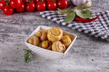 Fototapeta premium Pickled mushrooms in white bowl with cherry tomatoes and herbs on rustic surface