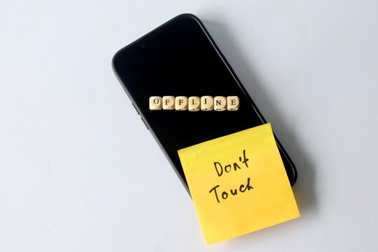 High-angle minimalist view of a smartphone on a white surface with "OFFLINE" letter cubes and a "Don't Touch" note, featuring ample copy space.