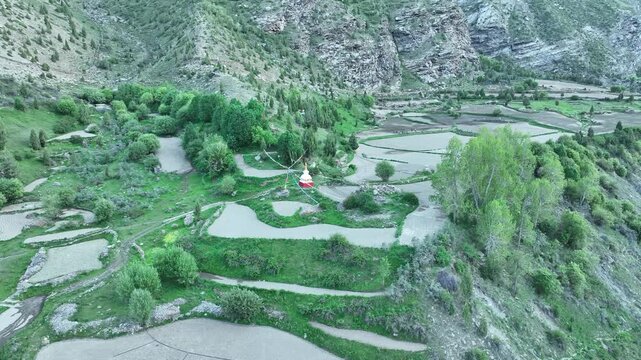 Aerial view of Buddhist stupa decorated with colorful prayer flags on a cliff edge in the Himalayas near Jispa Lahaul Valley shot by a drone

