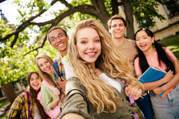 Fototapeta premium Group of smiling college students taking a campus selfie together, diverse young friends enjoying outdoor university life and studying with notebooks