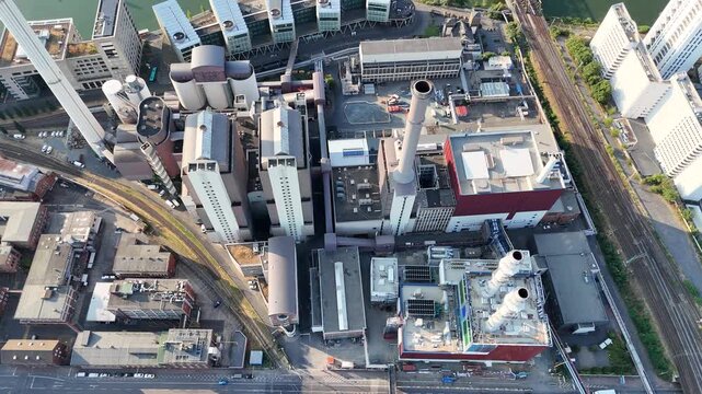 Aerial view of an industrial power plant complex featuring tall chimneys, factory buildings, and adjacent railway tracks in the urban landscape of Frankfurt am Main, Hessen, Germany.