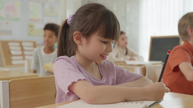 Young Girl Writing With Pencil at Classroom Desk, Elementary School Student and Child Study Education Lesson, Classmates Learning Together in Cheerful Warm Daylight, Focused School Activity