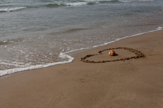 Heart drawn in beach sand with seashell near the waves