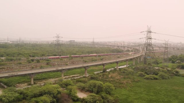 Aerial view of a moving train on a bridge near high voltage power lines in Delhi NCR India