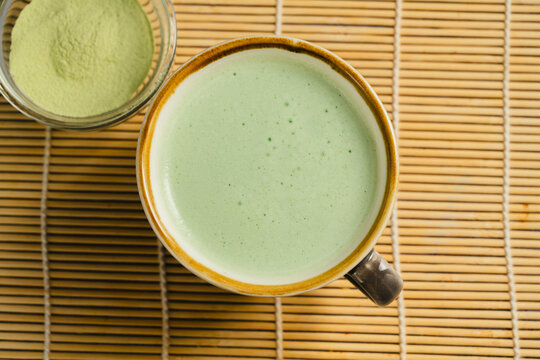 Matcha latte with green tea powder on bamboo mat, top view