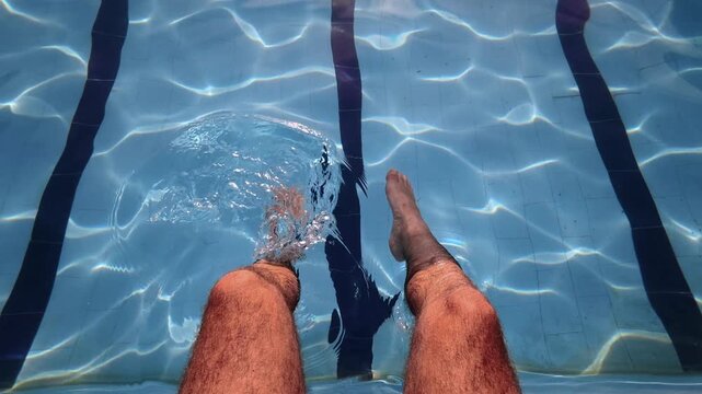 First person footage showing a man performing gentle aquatic exercises with his legs in a swimming pool.