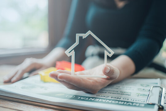 Green property investment and sustainable housing option concept, hand holding white house model over environmental corporate responsibility report for eco friendly real estate development choice