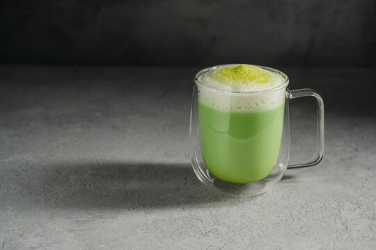 Matcha latte with frothy milk and green tea powder in glass cup. Healthy food, nutrition and antioxidant on dark background with copy space