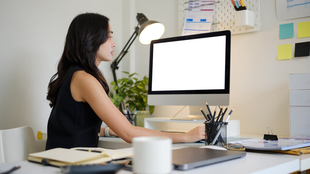 Young Asian businesswoman working at a desktop computer with a blank screen.