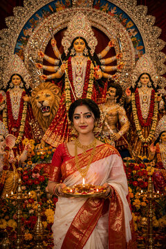Indian woman holding a diya plate before Goddess Durga idol during Durga Puja religious celebration