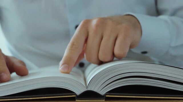Close-up of a person consulting a law book and pointing at legal text to research legislation and regulations.