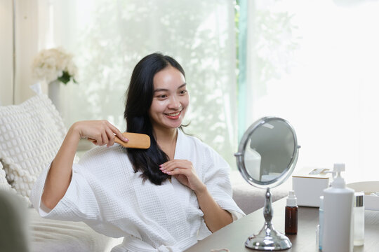 Young Asian woman brushing her hair during a home beauty routine.