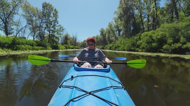 Mature woman in tandem kayak resting and holding paddle on river POV