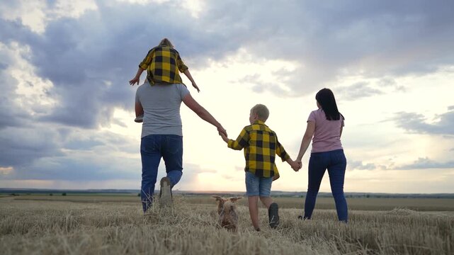 Happy cute family. Hiking outdoors in wheat field. Family walk together holding hands in natural park. Picnic in countryside at sunset. Children with parents walk with pet. Summer outdoor recreation.
