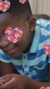 Animation of heart icons with flowers over african american reading book