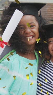 Animation of gold confetti over happy diverse schoolgirls with diplomas and mortar boards embracing