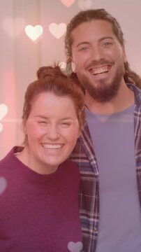 Animation of hearts over happy diverse couple at home