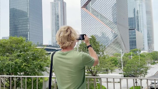 Young Man Using Smartphone Against Skyscrapers &ndash; Talking, Scrolling or Recording Video