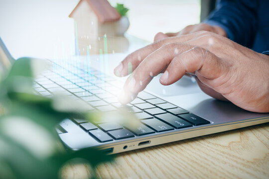 Business professional typing on laptop keyboard with holographic financial data growth charts and house model, concept of real estate investment analysis, property market report, and housing finance.