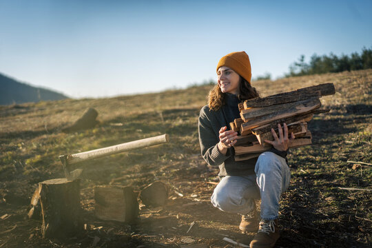 Happy young woman holding a handful of firewood logs. Cozy winter lifestyle.